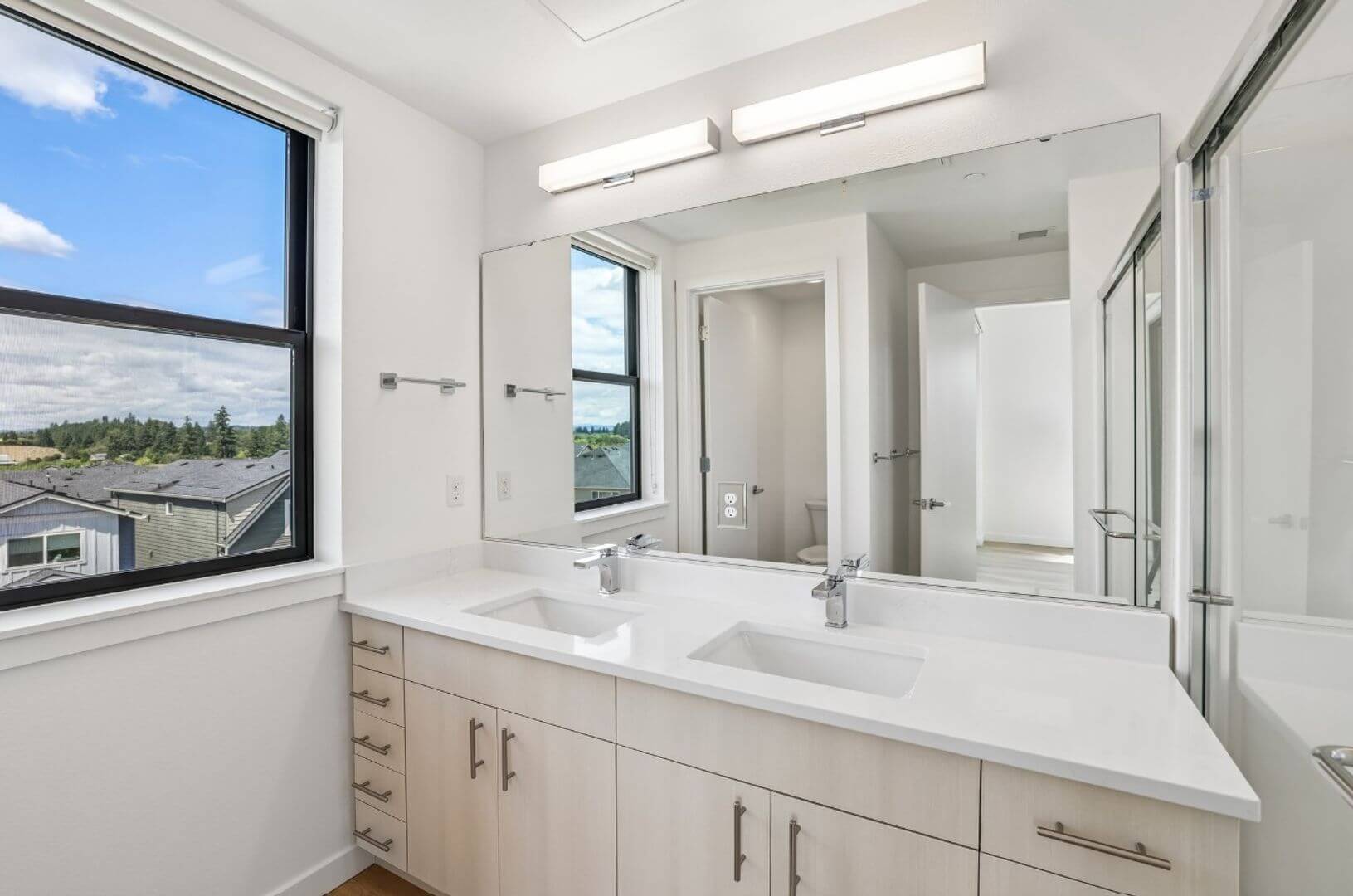 Primary bathroom with dual vanity, glass shower, and window views